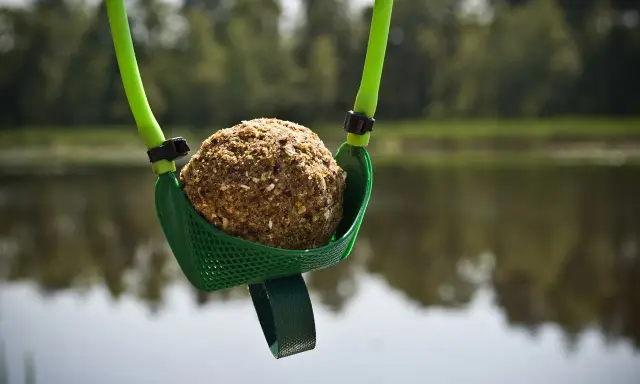 Zielona proca do zanęty z kulką zanętową gotowa do rzutu nad spokojną wodą.