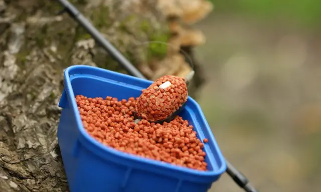 Niebieskie pudełko z zanętami Lorpio feeder, gotowe do akcji. Wędka w tle.
