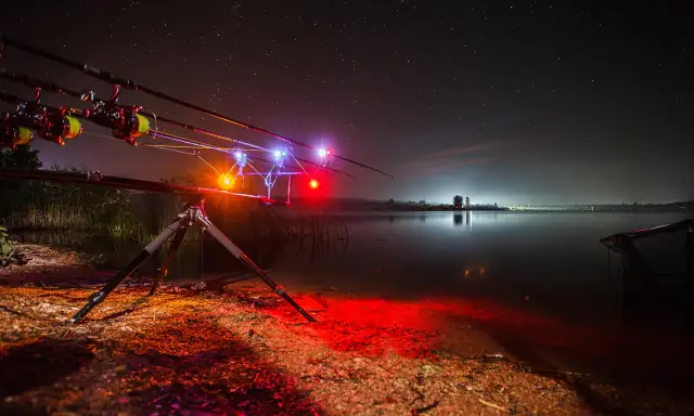 Nocne łowienie karpi. Wędki na podpórce z sygnalizatorami brań, jezioro i gwiazdy. To jak zrobić świetlik na ryby.
