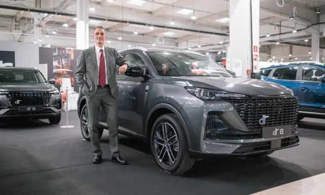 Mężczyzna w garniturze opiera się o szare auto DR 6. Obok stoi DR 5.