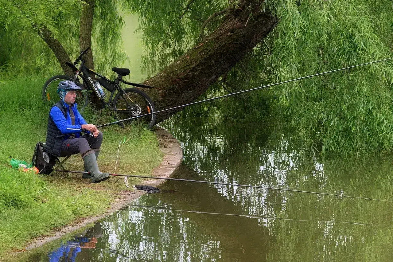 Wędkarz czeka na branie, rower obok. Jak zastawić żak na ryby? Spokojny dzień nad wodą.