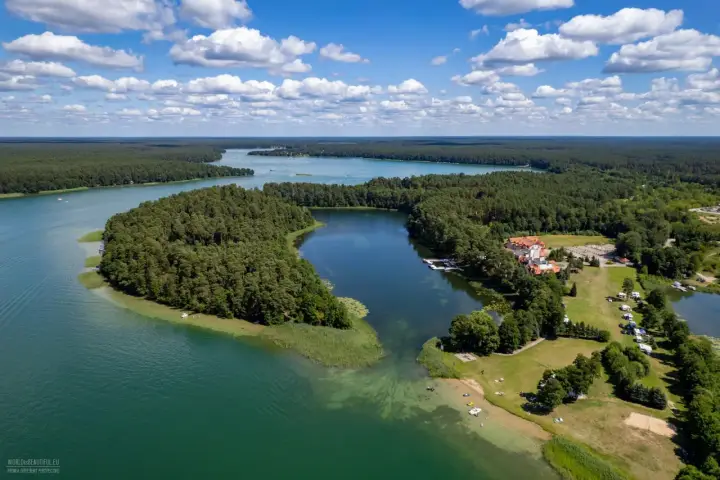 Malownicze jezioro Lechickie otoczone lasem, z hotelem i polem kempingowym na brzegu.